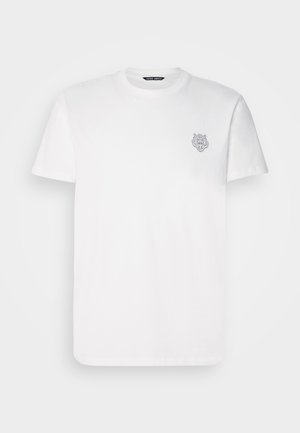 Camiseta de algodón blanca de manga corta y cuello redondo. Tiene un pequeño diseño gráfico gris de la cabeza de un león en el lado izquierdo del pecho.
