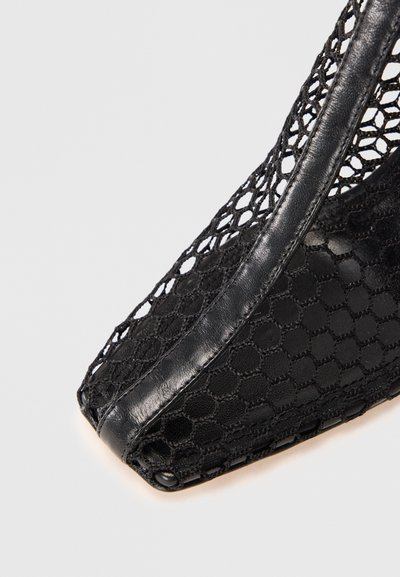 Scarpa in mesh nero con rifiniture in pelle e punta affilata, che mostra un primo piano dei dettagli della texture e della cucitura su sfondo bianco.