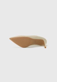 Glittery gold high heel shoe with a pointed toe and slim stiletto heel, featuring a textured brown rubber sole.