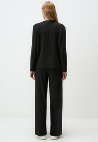 Maglione nero lavorato a maglia e pantaloni larghi, caratterizzati da una texture a coste e una vestibilità rilassata. Il maglione ha un semplice colletto a girocollo, mentre i pantaloni sono senza cuciture all'orlo.