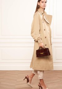 Beige trenchcoat met grote knopen, handtas met een bruine krokodillenprint, crèmekleurige broek en naaldhakken in een nude kleur. Soepele texturen door het geheel.