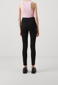 Jeans negros de cintura alta con un diseño ajustado y bolsillos traseros. Combinados con una blusa sin mangas de punto rosa y zapatos negros con tachuelas.