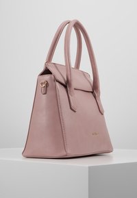 Růžová kožená kabelka se strukturovaným tvarem, dvojitými uchy a překlápěcím uzávěrem. Vybavena zlatými kovovými akcenty a texturovaným povrchem.