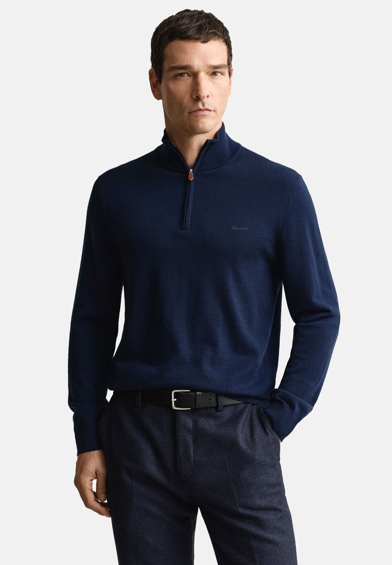 Marineblauwe trui met kwart-ritssluiting van zacht materiaal met lange mouwen, voorzien van een subtiel logo op de borst en gecombineerd met op maat gemaakte donkere broek.