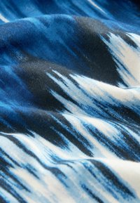 Gros plan sur un tissu bleu, noir et blanc avec un motif tie-dye montrant la texture et les plis.