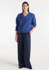 Suéter azul, peludo y de gran tamaño con cuello en V, combinado con pantalones de pierna ancha a rayas marino. Textura suave, corte relajado y estilo casual.