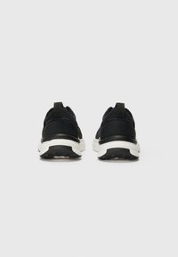 Scarpe da ginnastica nere con una finitura liscia e opaca, una suola intermedia bianca e una suola nera testurizzata, complete di linguette sul tallone.