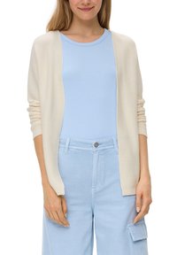 Lichte, open voorkant cardigan in crème, met een gestructureerde brei. Gegdraag over een lichtblauw top en gecombineerd met lichtblauwe broek met zakken.
