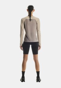 Beige Langarm-Lauftop mit passgenauer Schnittführung, strukturiertem Rücken, kombiniert mit schwarzen Radsportshorts und schwarzem Schuhwerk.