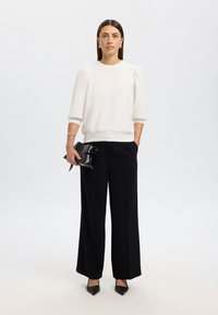 Hvit genser med lange ermer og rund hals, kombinert med høytlivede, svarte, vide bukser. Svart clutch med sløyfedetalj og spissede sko.