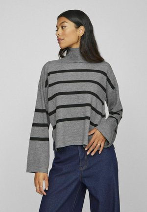 Haut à col roulé gris avec des rayures horizontales noires, coupe ample et manches larges. Le tissu semble doux et texturé.
