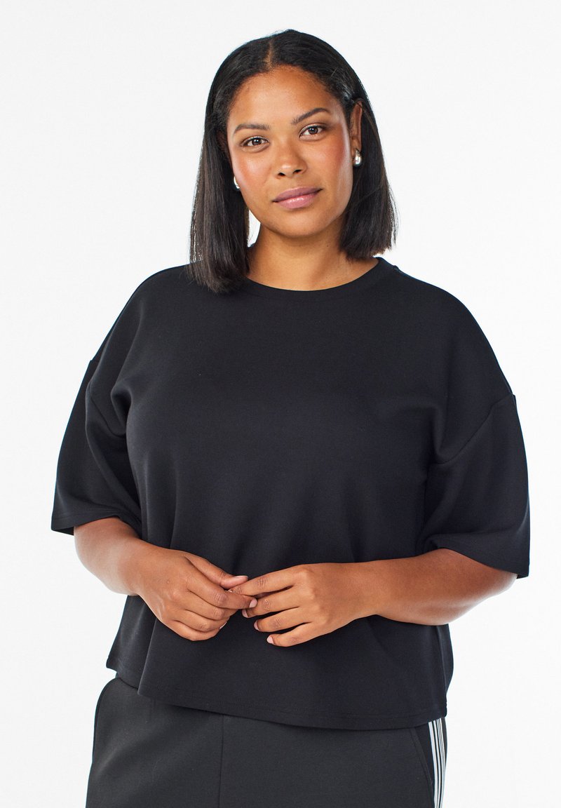 Juodas, per didelis trumpomis rankovėmis viršus, pagamintas iš minkštos medžiagos. Turi apvalią iškirptę ir laisvą kirpimą, tinkamą kasdieniam dėvėjimui.