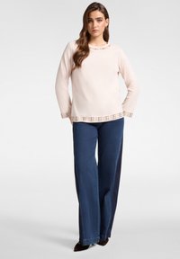 Maglietta a maniche lunghe rosa chiaro con un orlo decorativo di perline; abbinata a jeans a gamba larga blu scuro, creando un contrasto di colori e texture.