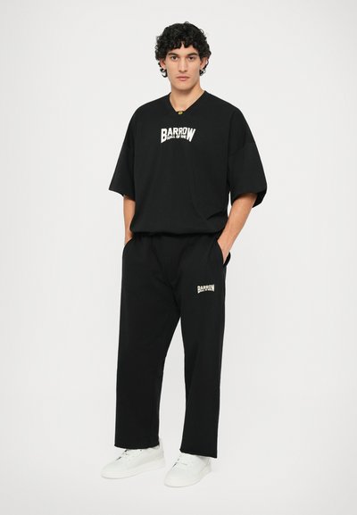 Black short-sleeve T-shirt and matching pants, both featuring a white "BARROW" logo. Model wears white sneakers. Simple, relaxed fit.