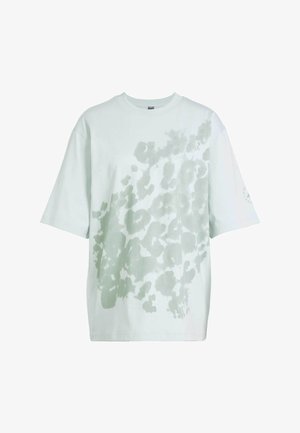T-shirt oversize vert clair en coton, comportant un motif abstrait flou dans une teinte plus claire sur le devant et des manches courtes.