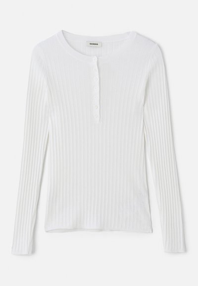 Fehér, hosszú ujjú, bordázott felső, kerek nyakkivágással és egy sor kis gombbal az elején. Simára textúrázott, testhezálló dizájn.