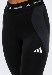 Μαύροι και σκουροί γκρι leggings συμπίεσης Adidas TECHFIT με εμφανές λογότυπο στο μηρό και ζωγραφισμένη ζώνη μέσης.