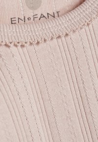 Helles rosa, geripptes Textil mit gewellten Kanten und feinen Nähten. Das Etikett trägt die Aufschrift "EN·FANT". Weiches, strukturiertes Material mit vertikalen Mustern.