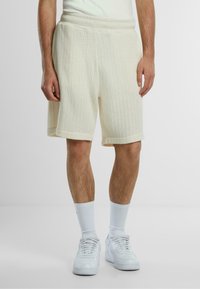 Kremfargede strikkede shorts med en teksturert ribbestruktur, med en bred livlinje og rullet kant, parret med hvite sokker og sneakers.
