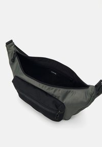 Grøn nylon skuldertaske med en sort frontlomme med lynlås. Rummeligt indre med en glat tekstur. Har justerbar rem og mærkelabel indeni.