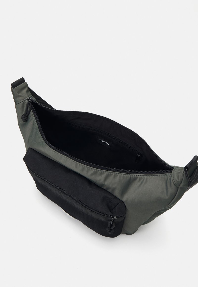 Bolso de hombro verde de nailon con un bolsillo frontal con cremallera negra. Interior espacioso con una textura suave. Incluye una correa ajustable y etiqueta de la marca en el interior.