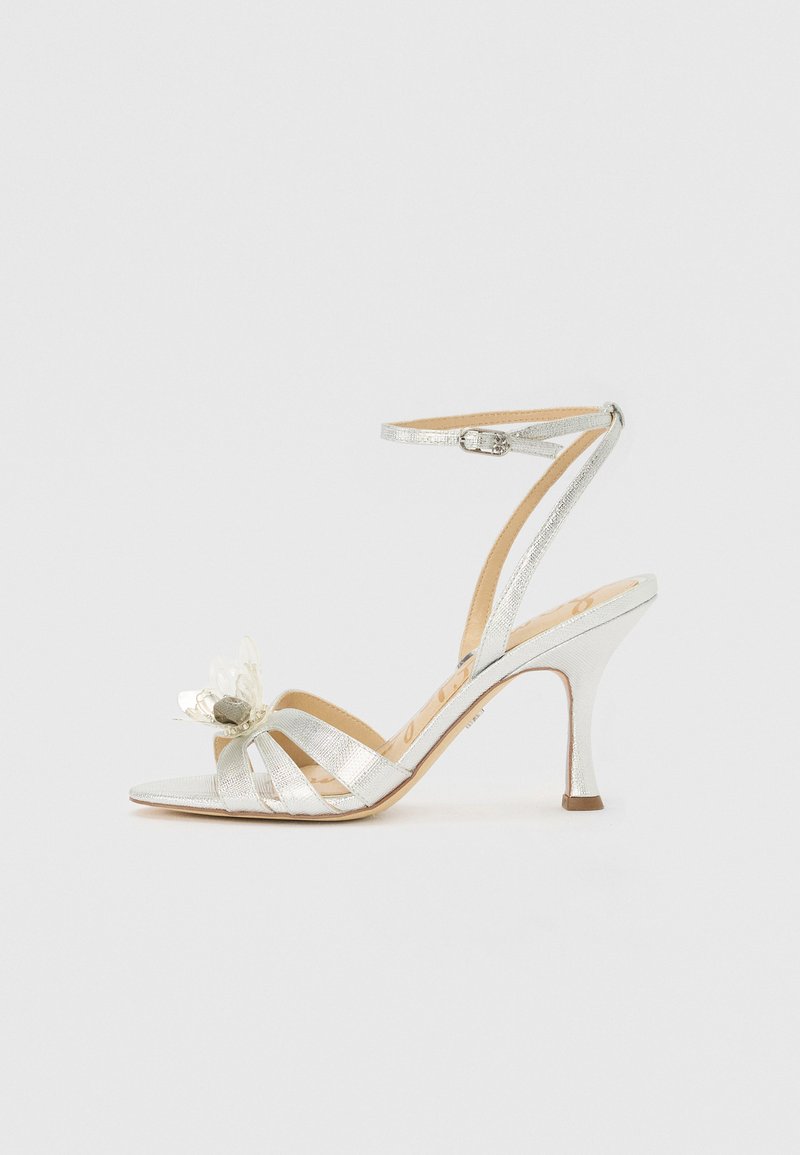 Stříbrné vysoké sandály na podpatku s špičatou špičkou, kotníkovým páskem a dekoračním vícestupňovým květinovým detailem vpředu. Hladký povrch.