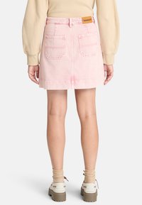 Gonna di jeans rosa con tasche posteriori, taglio dritto e etichetta del produttore visibile sulla vita. Il tessuto ha una consistenza liscia.