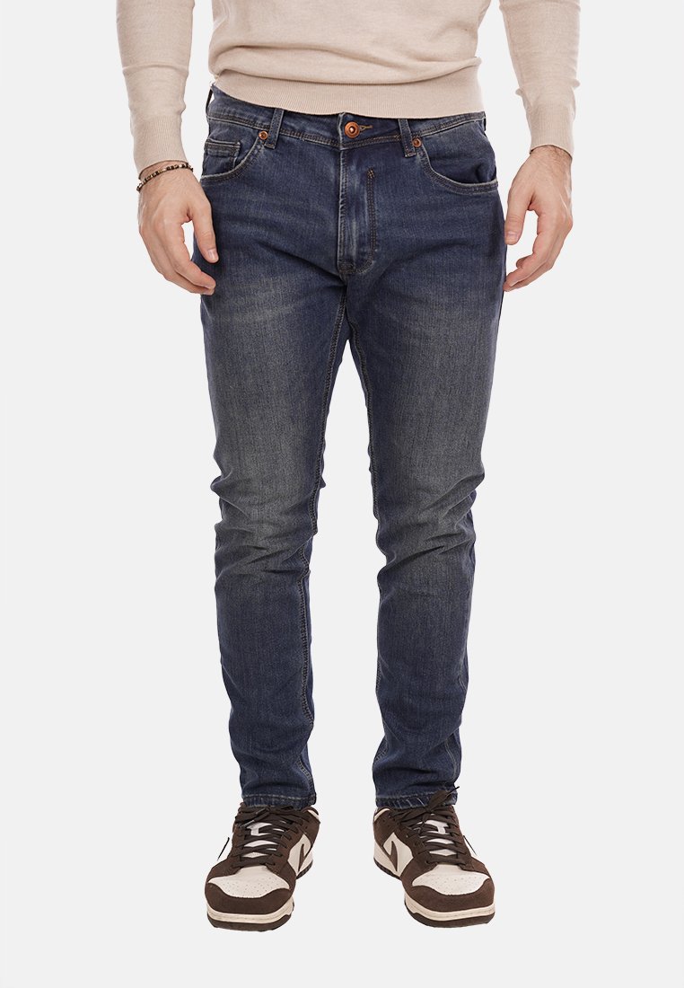 Jeans in denim blu scuro con vestibilità slim, design a cinque tasche e leggera scoloritura, abbinati a sneakers marroni e bianche.