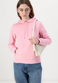 Sweat à capuche rose avec poche avant, manches et ourlet côtelés. Associé à un jean en denim bleu. Présentant un léger sac avec une bandoulière.