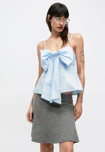 Svetlomodrý tielkový top s veľkou mašľou vpredu, vyrobený z bavlny. Kombinovaný so sivou vlněnou sukňou s jemným áčkovým strihom.