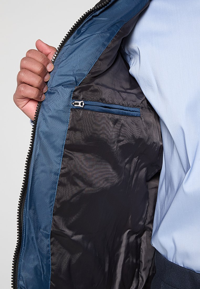 Doublure de veste bleu marine avec une texture lisse, dotée d'une poche zippée. Le tissu extérieur est résistant avec un fini brillant.