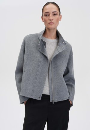 Grey wool jacket with a structured design, high collar, and front zipper. Features snap closures and a soft texture, paired with a light sweater.