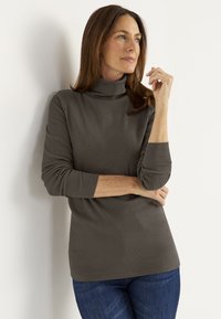 Gray ribbed turtleneck top with long sleeves, featuring a relaxed fit. Worn with dark blue jeans, displayed against a white background.