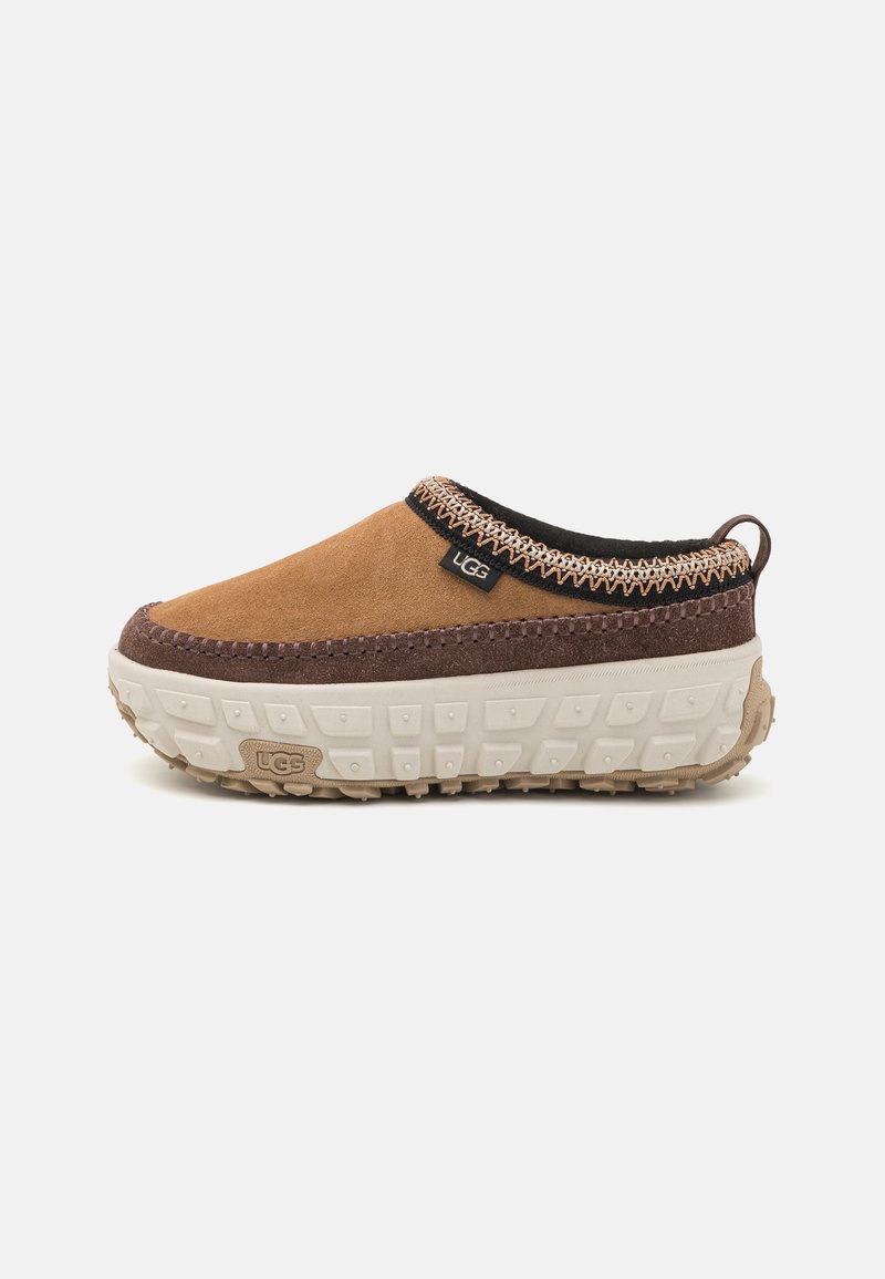 Bruine nubuck instapschoen met een gestructureerde donkerbruine tussenzool, zwarte kraag en decoratieve stiksels, voorzien van een witte rubberen loopzool.