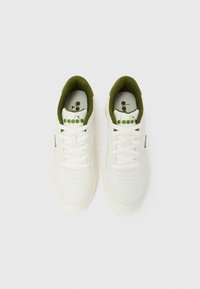 Paar weiße Sneakers mit grünem Innenfutter und grünem "diadora"-Logo auf der Zunge, von oben auf einem einfarbigen Hintergrund gesehen.