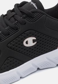 Svart träningsskor med texturerat mesh-övre, med perforerade detaljer, en vit sula och en liten logotyp på sidan.