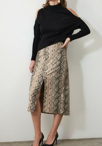 Pull noir à épaules dénudées assorti à une jupe beige à motif serpent arrivant au genou avec une fente à l'avant. Chaussures noires à talons hauts.