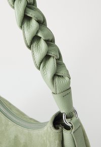 Bolsa de mão verde em couro com uma alça trançada, textura suave, detalhes em metal prateado e um fecho de correr na borda superior.