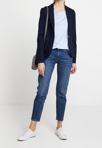 Marynarski blezer, jasnoniebieska koszulka i ciemnoniebieskie dżinsy. Białe trampki i mała szara torebka. Casualowy, dopasowany krój i gładkie tekstury.