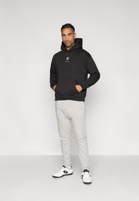 Sweatshirt preta com capuz e bolso frontal, calças de fato de treino cinza e ténis desportivos brancos. Design simples, ajuste casual e marcações mínimas.