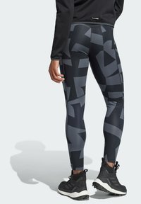 Zwart-grijs gemarmerde legging van rekbaar materiaal, met een hoge tailleband en een gladde textuur, gecombineerd met zwarte sportschoenen.
