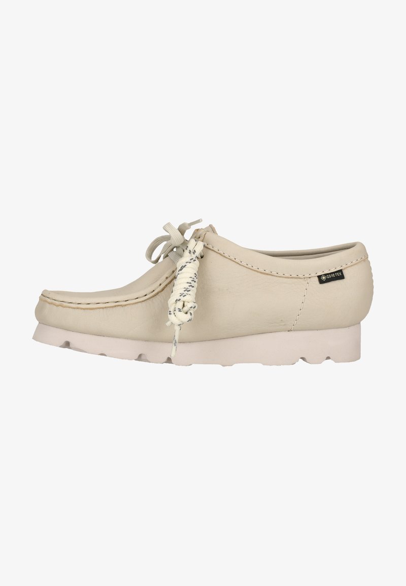Mocassin en cuir beige avec semelle blanche, nœud de lacet et étiquette en tissu Gore-Tex sur le côté.