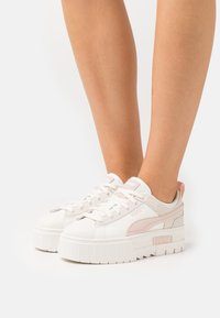 Baskets Puma avec une tige en cuir blanc, des accents roses, une texture lisse et une semelle épaisse en caoutchouc blanc. Conception à lacets avec un logo sur le côté.