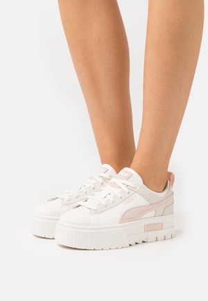 Baskets Puma avec une tige en cuir blanc, des accents roses, une texture lisse et une semelle épaisse en caoutchouc blanc. Conception à lacets avec un logo sur le côté.