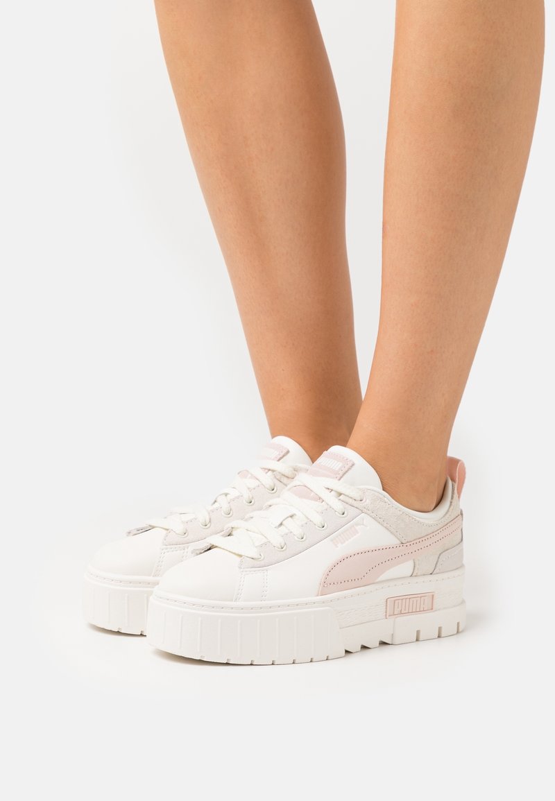 Baskets Puma avec une tige en cuir blanc, des accents roses, une texture lisse et une semelle épaisse en caoutchouc blanc. Conception à lacets avec un logo sur le côté.