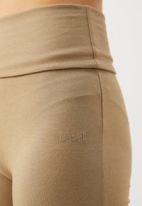 Kávové legíny s vysokým pásom, vyrobené z hladkého, elastického materiálu. Obsahujú diskrétny vyšitý logo "Casall" po boku.