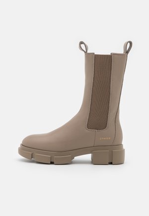 Taupe læderstøvle til midt på læggen med chunky sål, elastiske sidepaneler, trækflapper og "CPNHGN" guldtekst nær hælen.