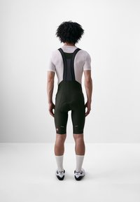 Zwarte fiets-bibshorts met meshbandjes, gevoerde rug en reflecterende accenten; gecombineerd met een witte mesh basislaag en witte sokken.