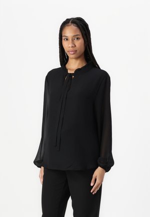 Black blouse made of lightweight fabric, featuring a ruffled neckline, long sleeves, and a keyhole front with ties. Smooth texture.