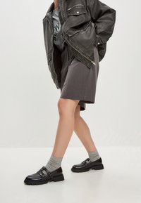 Černá umělá kožená bunda s prošívanou podšívkou, šedá košile, šedá midi sukně a černé boty s přezkou a texturovanou podrážkou.